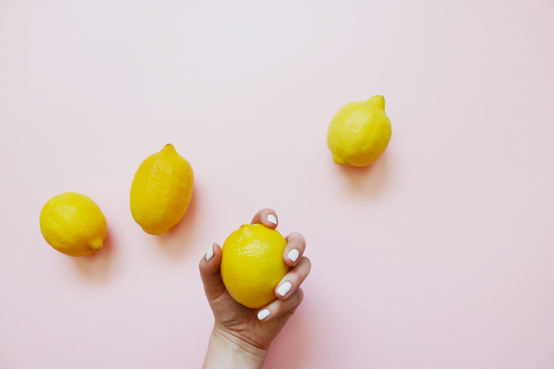A hand holding a bright yellow lemon on a soft pink background, symbolizing fresh approaches to clitoral stimulation.