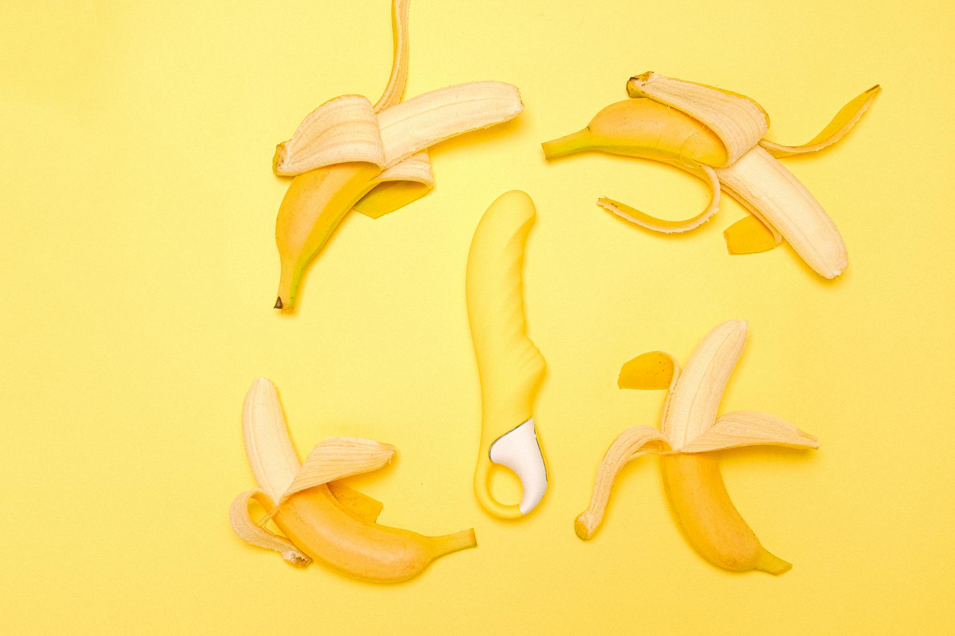 A yellow silicone lemon vibrator surrounded by peeled bananas on a yellow background