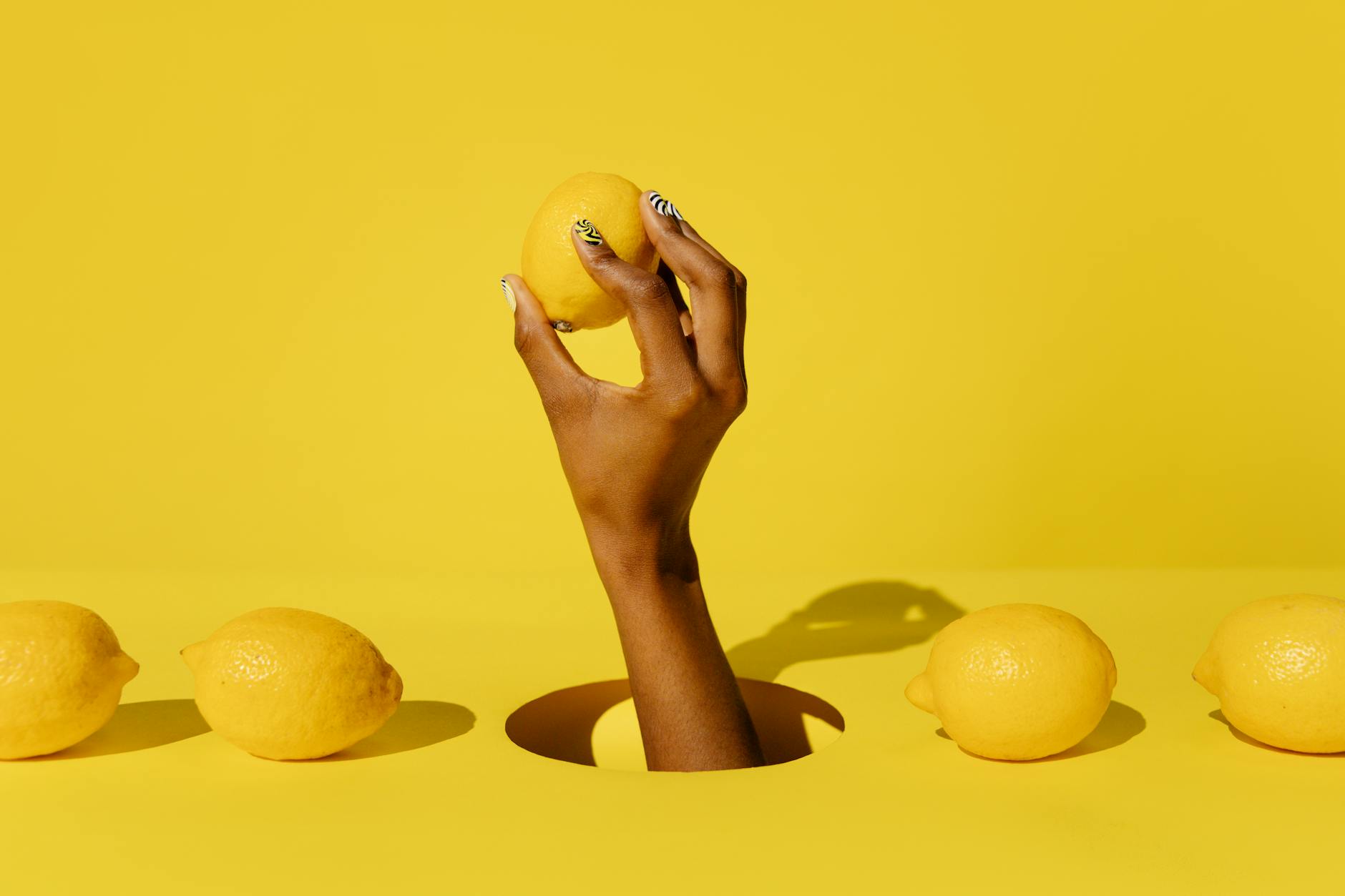 A hand holding a vibrant yellow lemon against a bright yellow background, symbolizing fresh, pressure-free pleasure