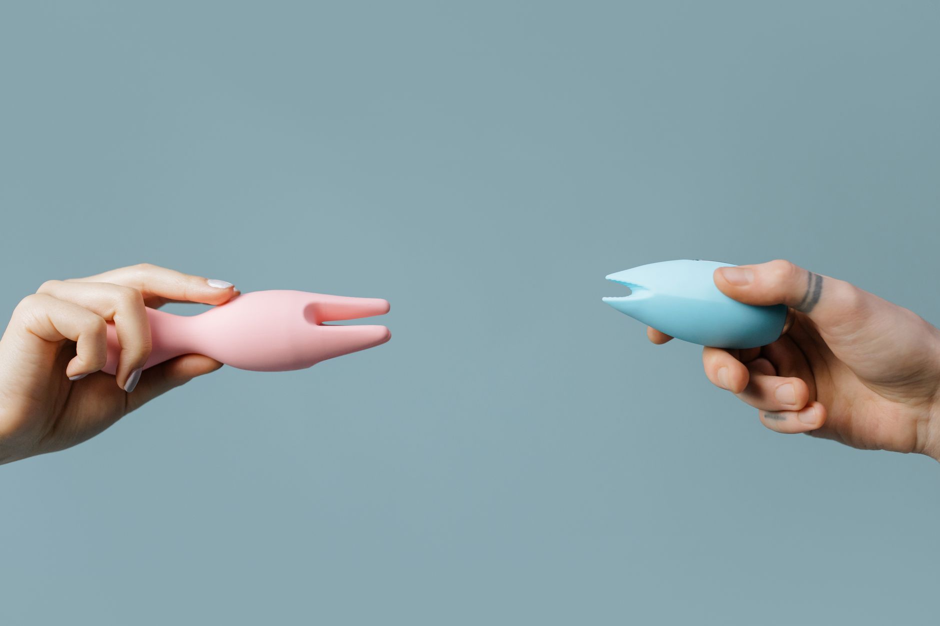 A blue silicone clitoral vibrator held gently in hand against a purple background, symbolizing self-care and personal healing