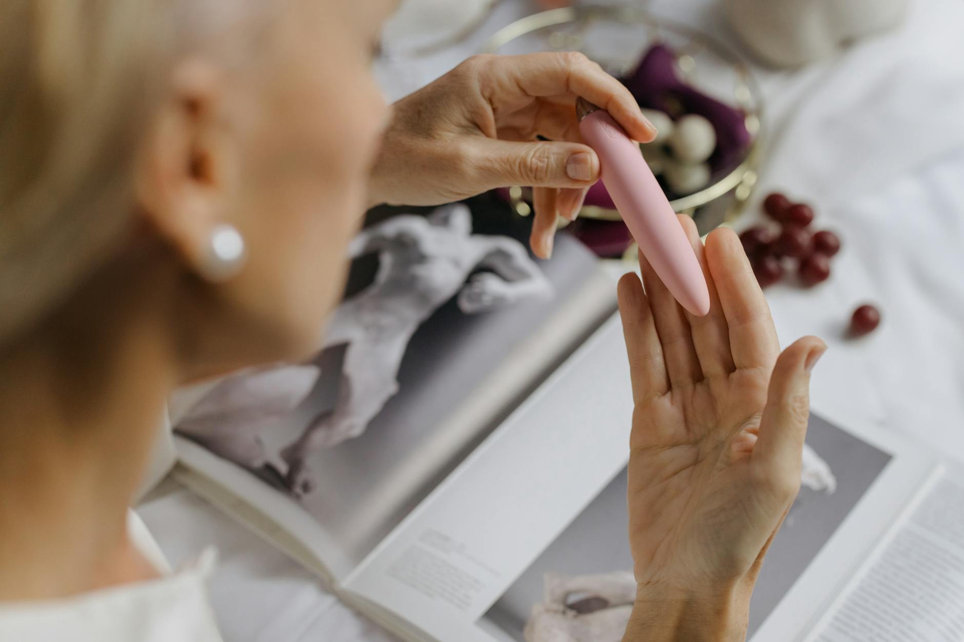 Close-up of a woman holding a vibrator with art books in the background, symbolizing informed self-care and intentional pleasure.