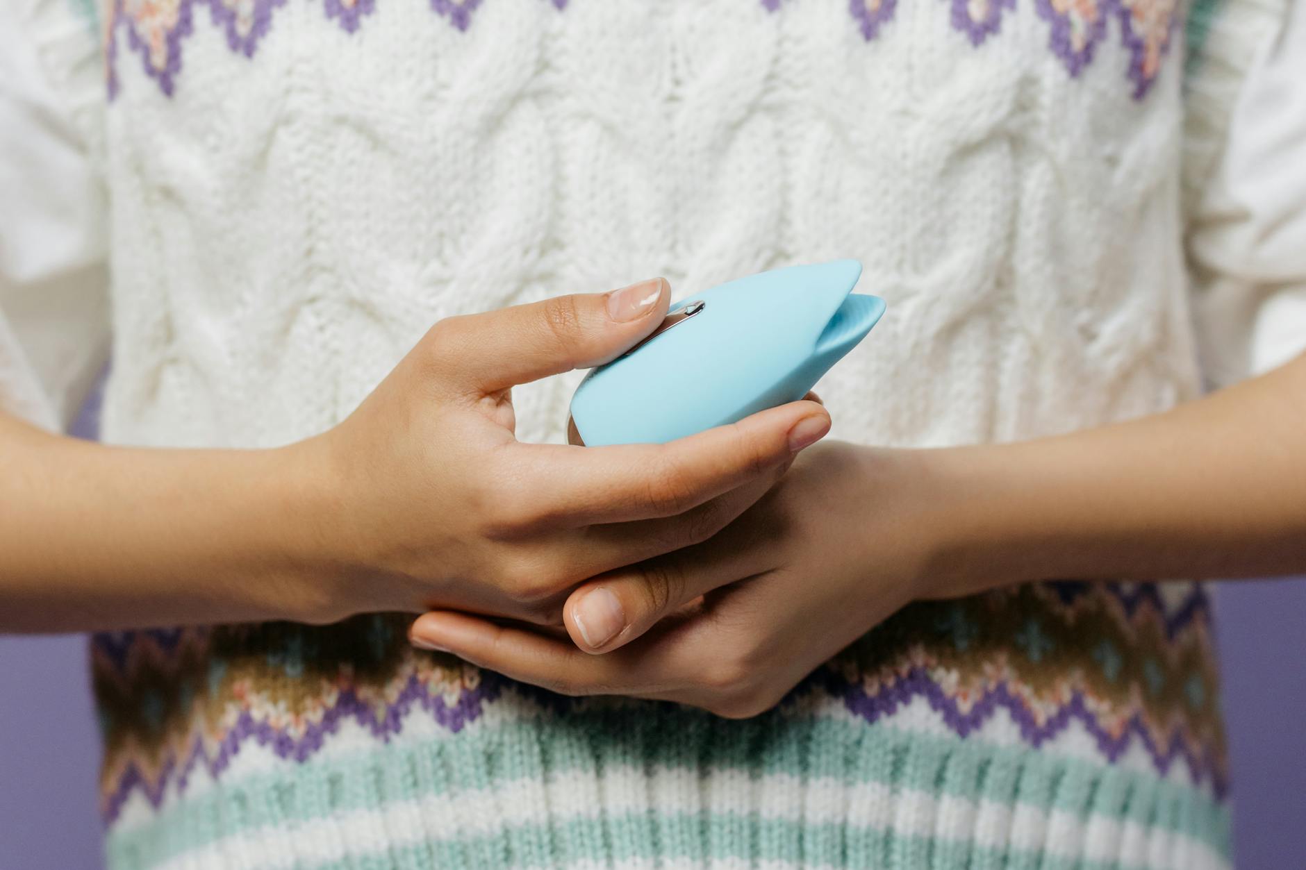 Close-up of hands holding a personal clitoral vibrator against a knitted sweater