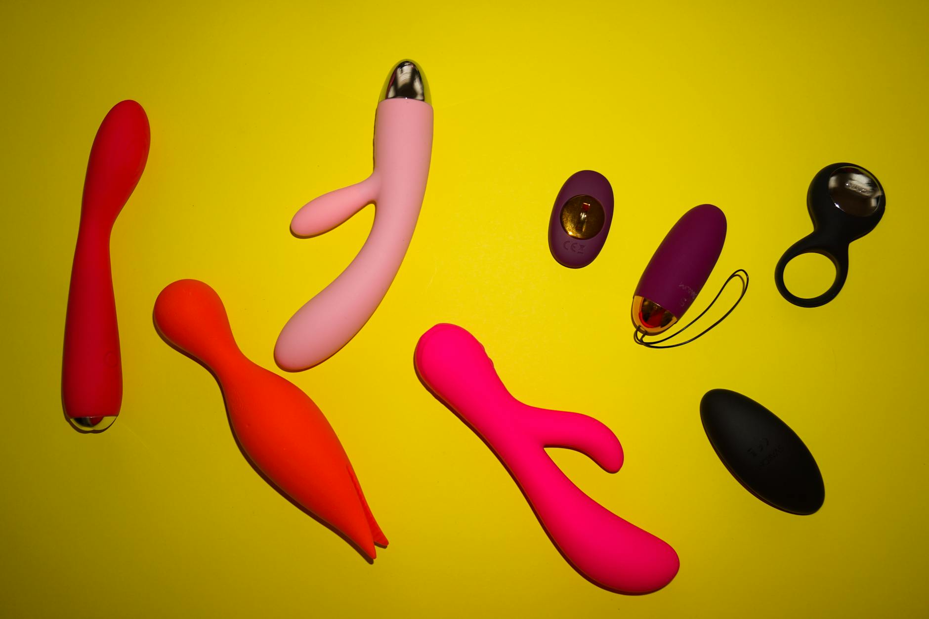 Colorful clitoral vibrators and adult toys displayed on a bright yellow surface, emphasizing design diversity and pleasure options.