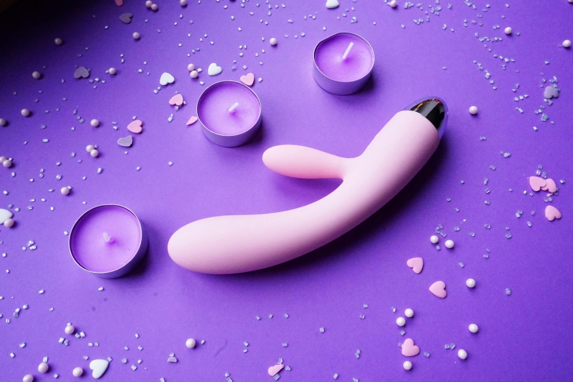Pink vibrator on purple background with heart confetti and candles, representing intimate connection between partners